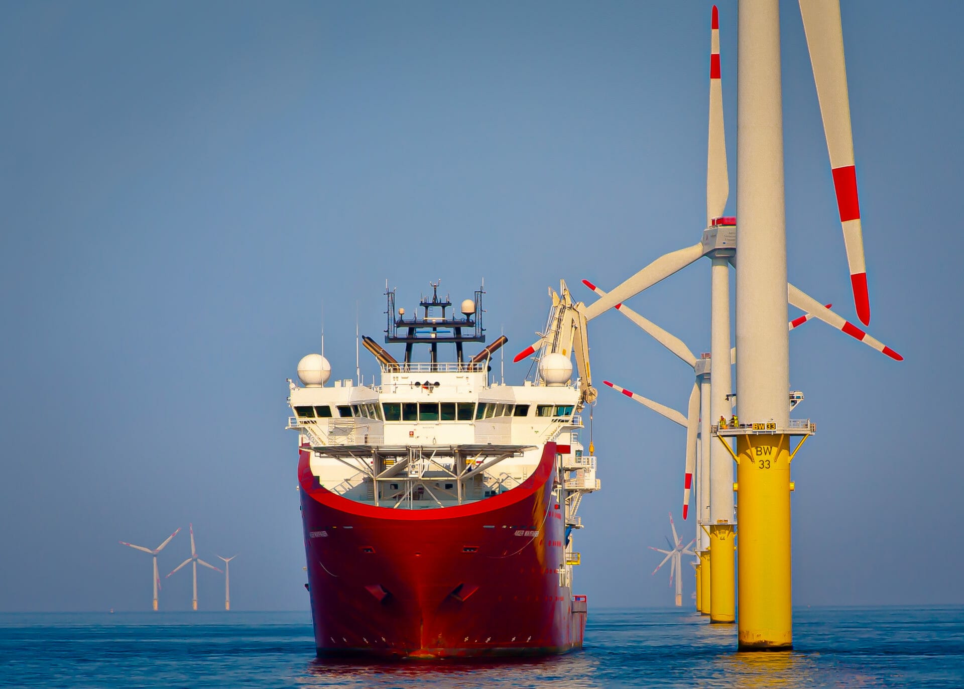 Ett rødt fartøy står ankret opp for å utføre service på en vindmølle installert i en vindmøllepark i havet.