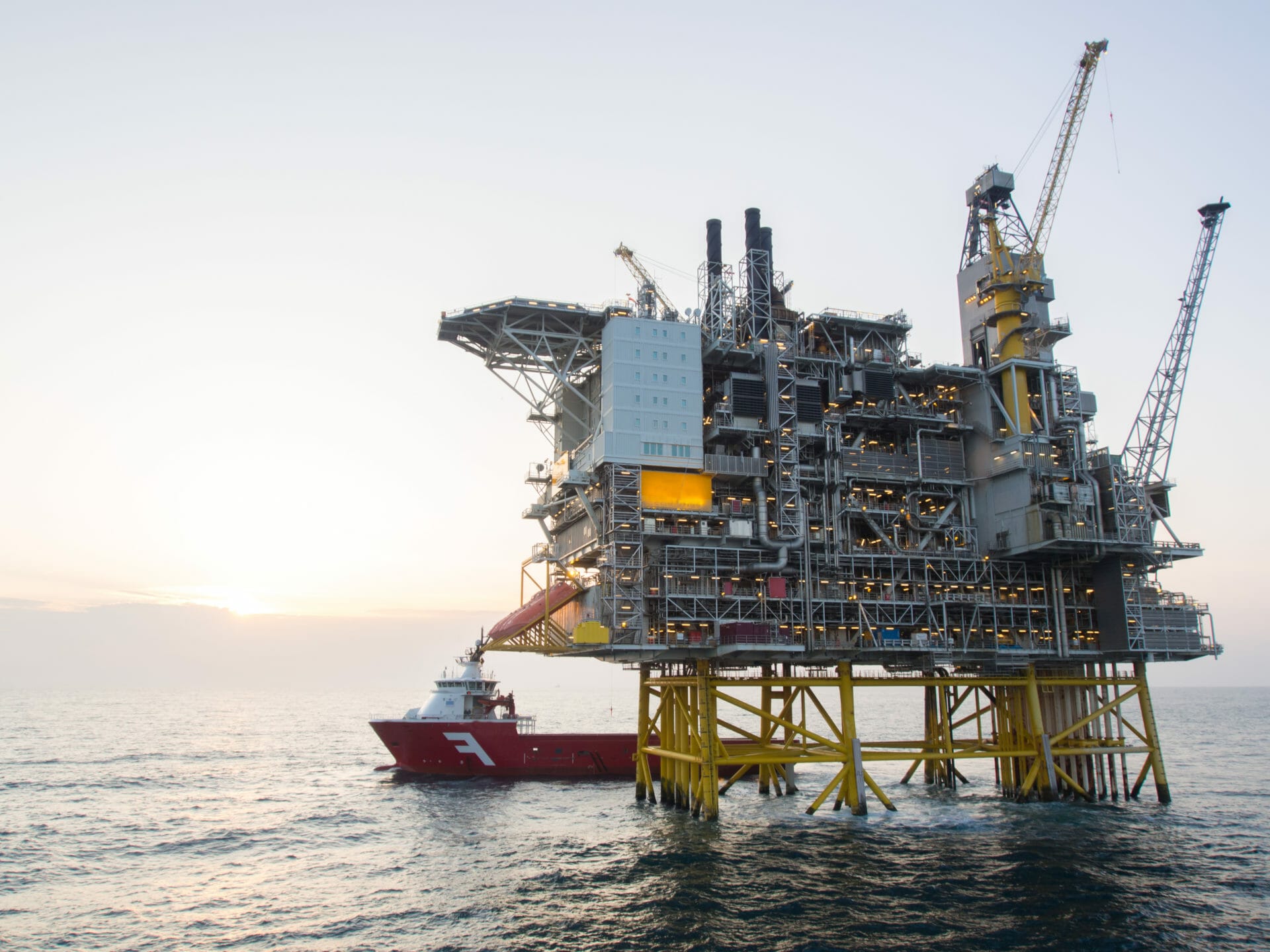 Olje og gass plattform i solnedgangen i Nordsjøen, et lasteskip ligger klart med forsyninger til plattformen.