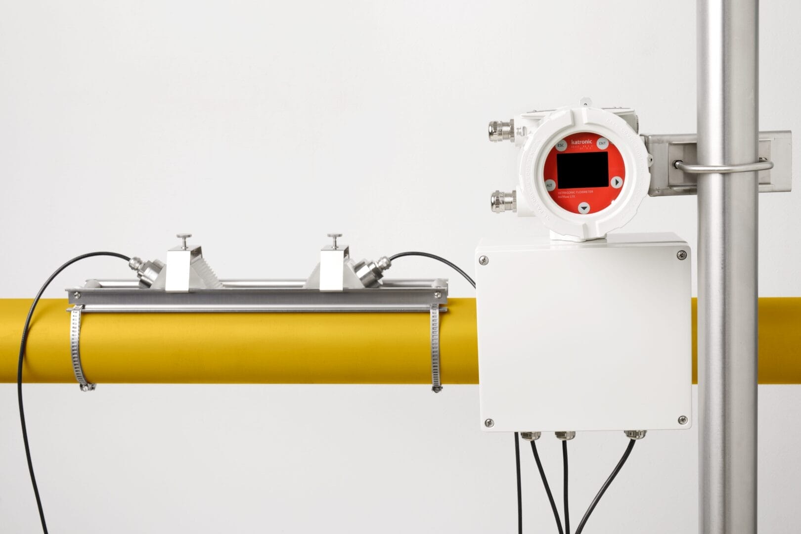 Fastmontert Katronic KATflow 170 ultralyd‑flowmeter installert på et gult prosessrør, med separat hvit koblingsboks og kabelføring samt en rektangulær metallramme festet over røret.