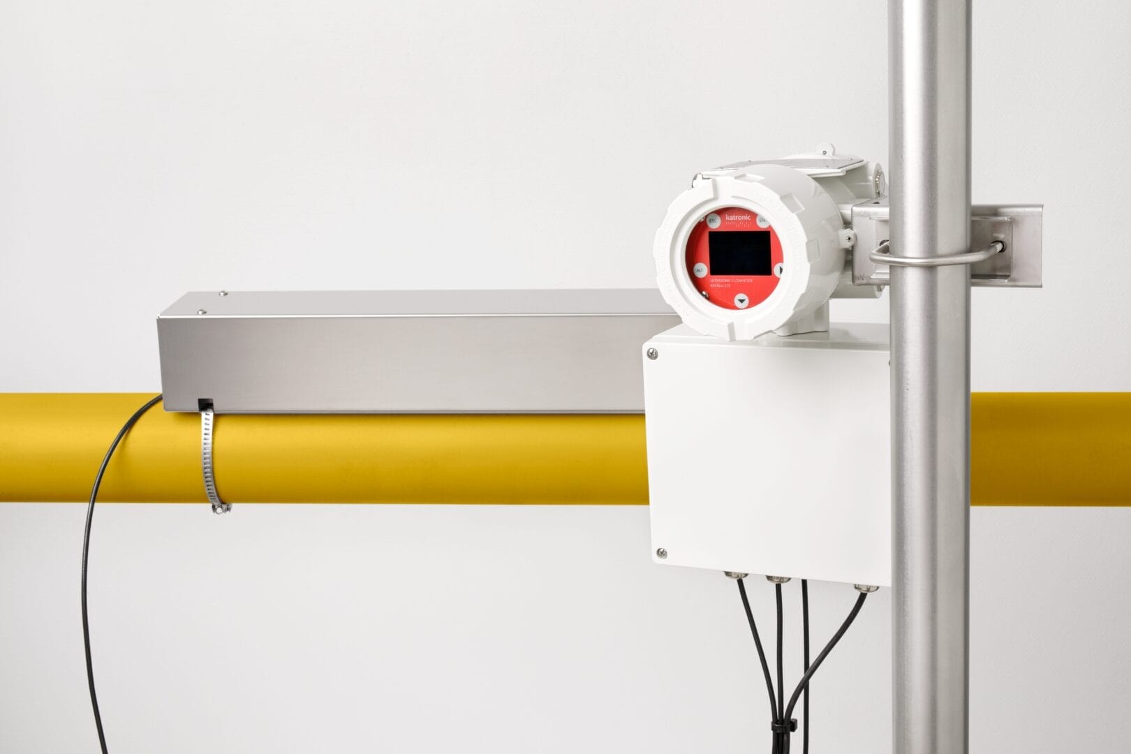 Katronic KATflow  ultralyd‑flowmeter montert på et gult rør, med rektangulær metallmodul festet over røret og en hvit koblingsboks under displayenheten, koblet til sensorer via kabler.