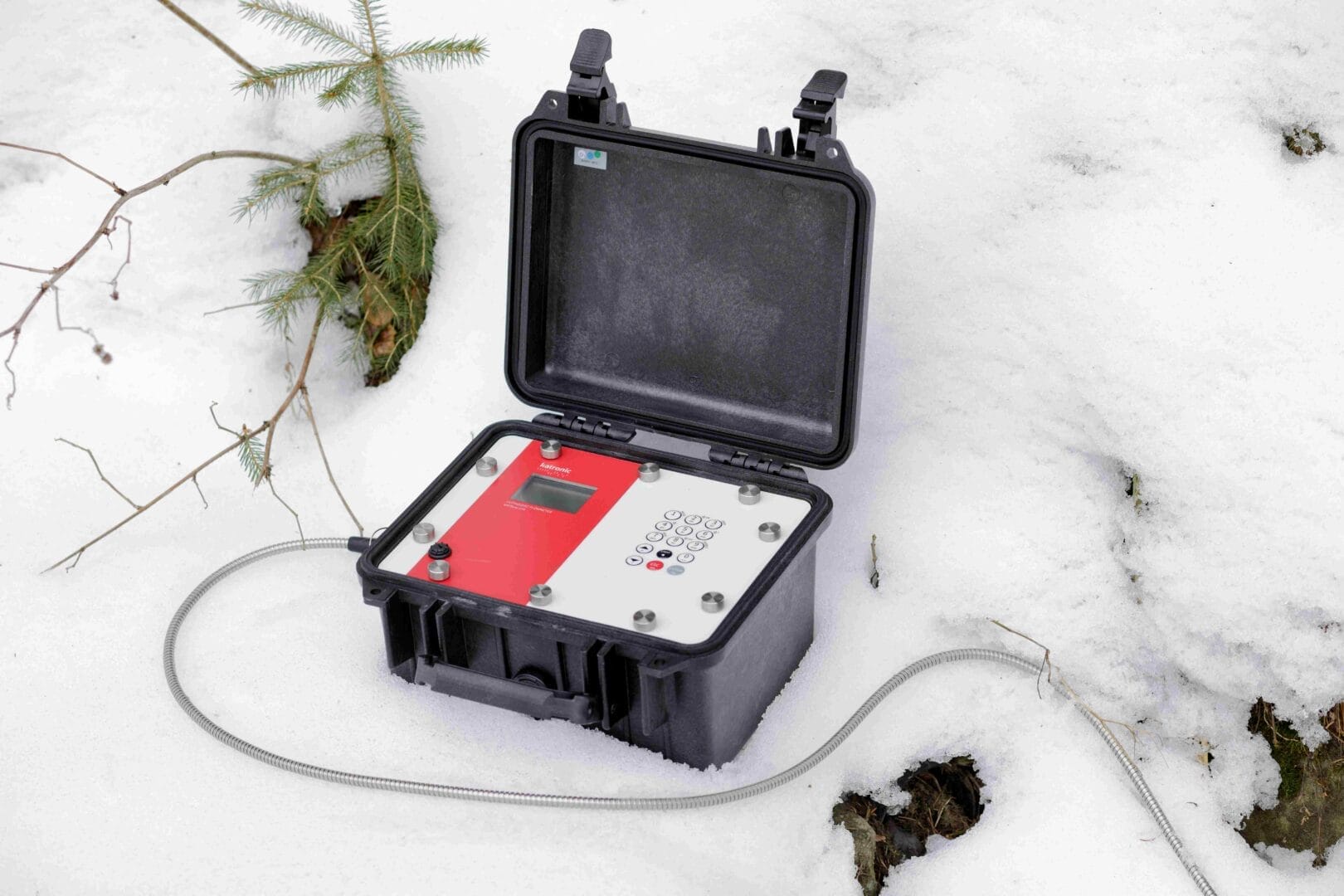 Portabelt Katronic ultralyd‑flowmeter plassert i en åpen, robust koffert på snødekt underlag.