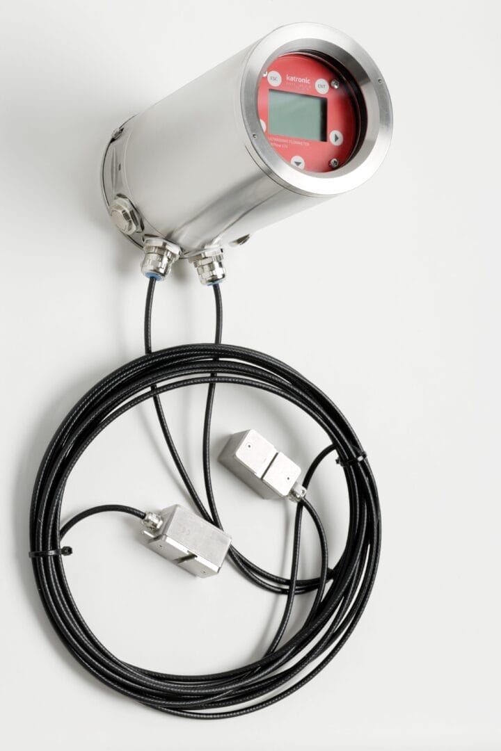 Ultralyd‑flowmeter av typen Katronic KATflow 170 med rund front, rødt displaypanel, LCD‑skjerm og fire betjeningsknapper i et robust metallhus med flere kabeltilkoblinger.