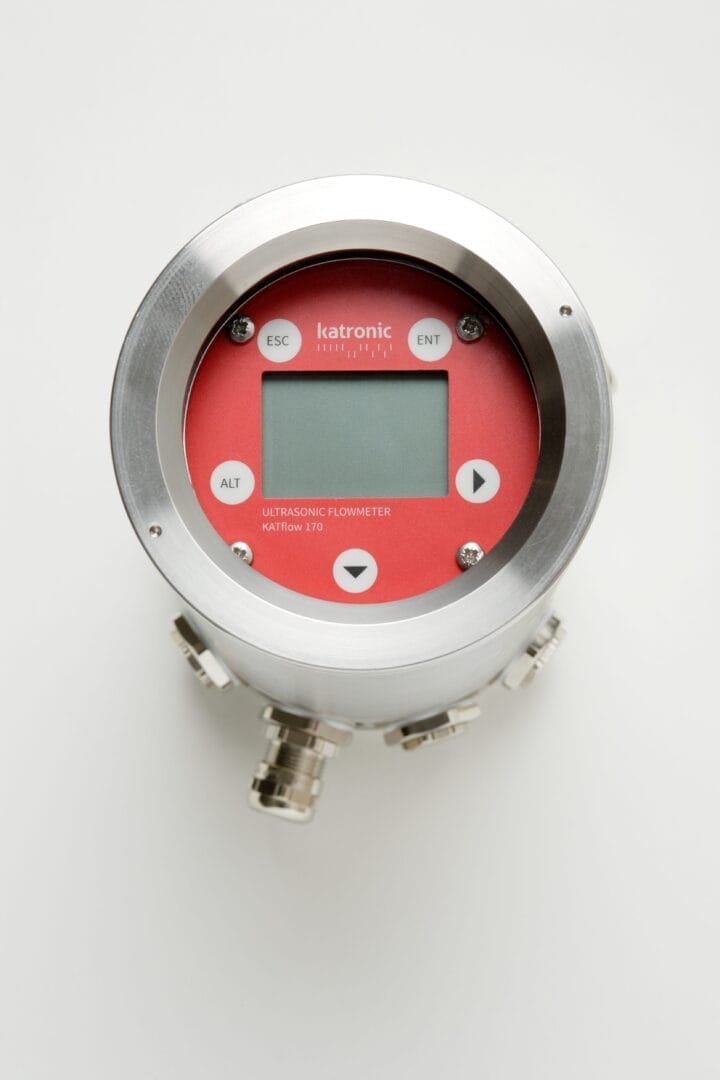 Katronic KATflow 170 ultralyd‑flowmeter i rund metallkapsling med rødt frontpanel, LCD‑display, fire betjeningsknapper og flere kabeltilkoblinger nederst.