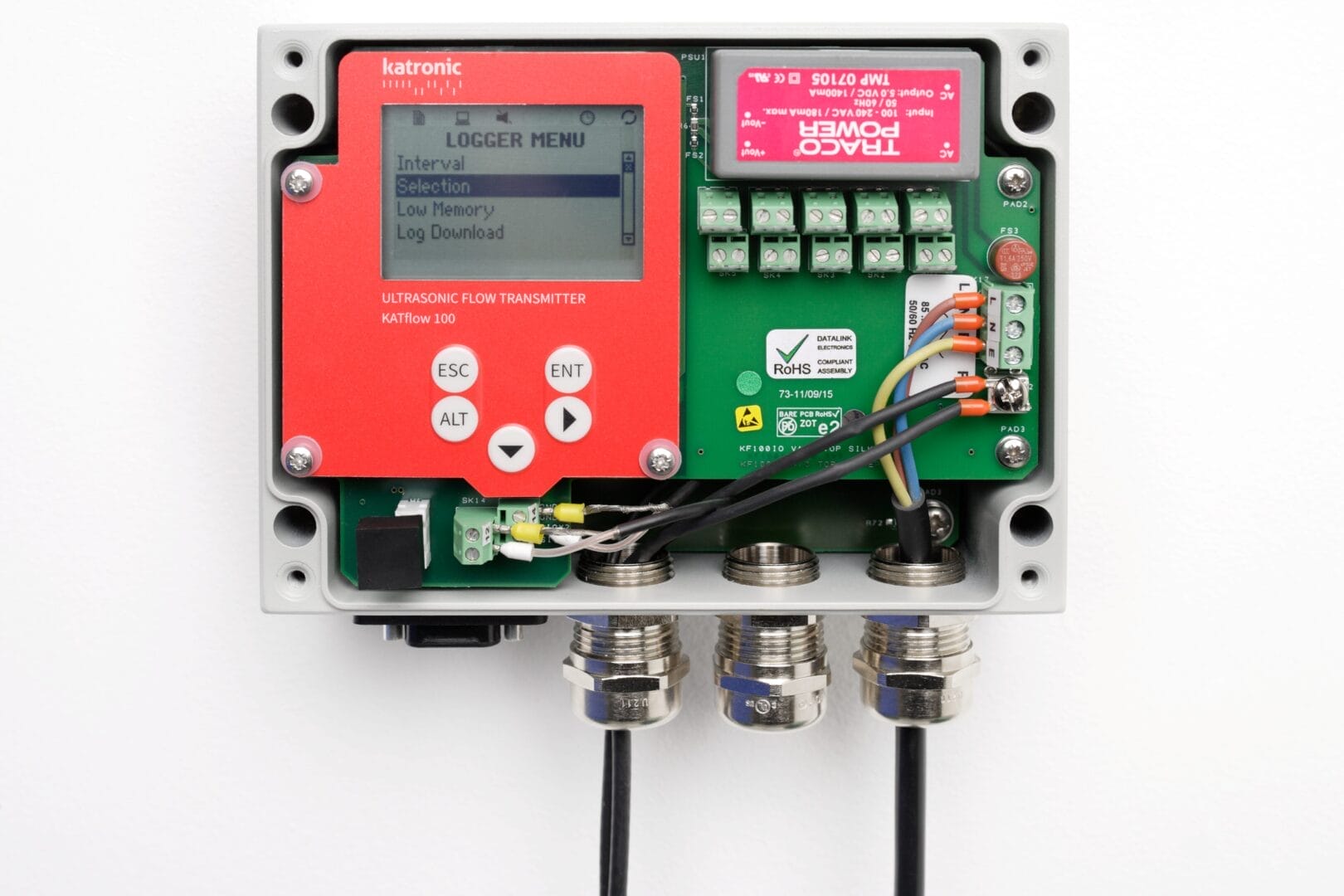 Åpen Katronic KATflow 100‑enhet som viser elektronikk, terminaltilkoblinger, display og kabelføringer inne i det rektangulære kapslede huset.